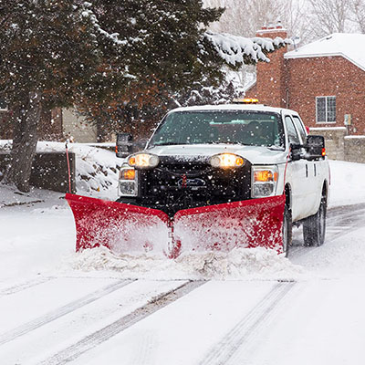 front image of white pickup truck with red snow plow on a snowy street